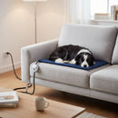 DreammyDoggie chew-resistant heating pad with digital control on a grey sofa, with a dog sleeping comfortably on top.