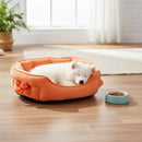 DreammyDoggie orange plush anti-anxiety princess dog bed with a bow detail, featuring a sleeping white puppy inside.